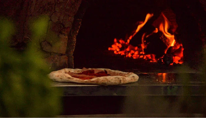 Pizza im traditionellen Holzofen mit leuchtenden Flammen und Edelstahlplatte